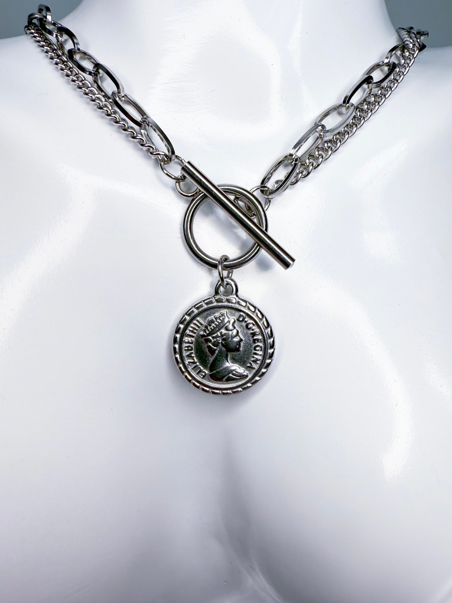 Silver coin necklace with a round pendant on a mannequin bust.