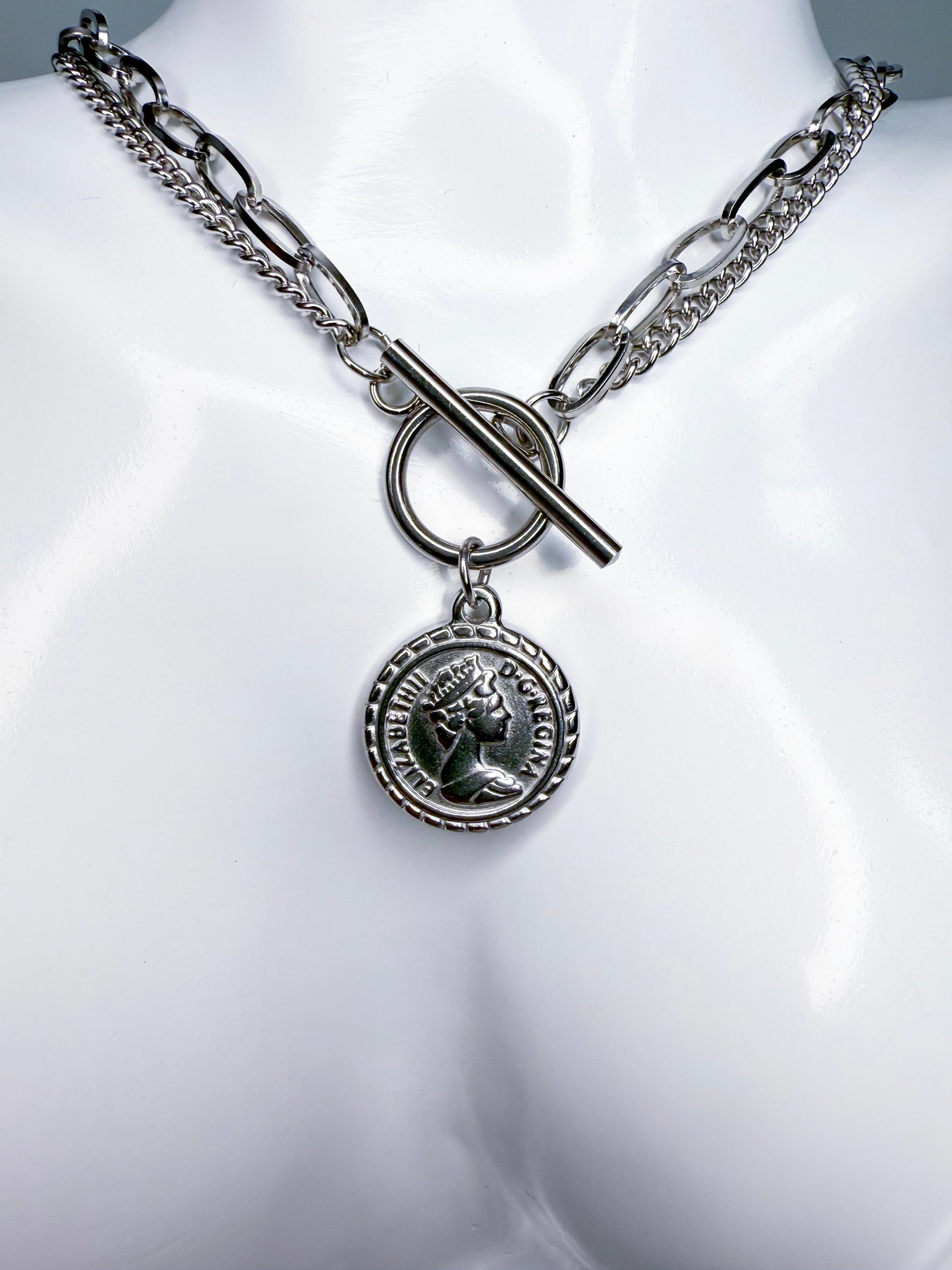 Silver coin necklace with a round pendant on a mannequin bust.