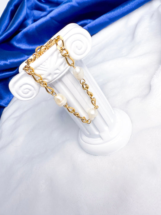 Gold chain earring with pearls on a white stand against a blue satin background