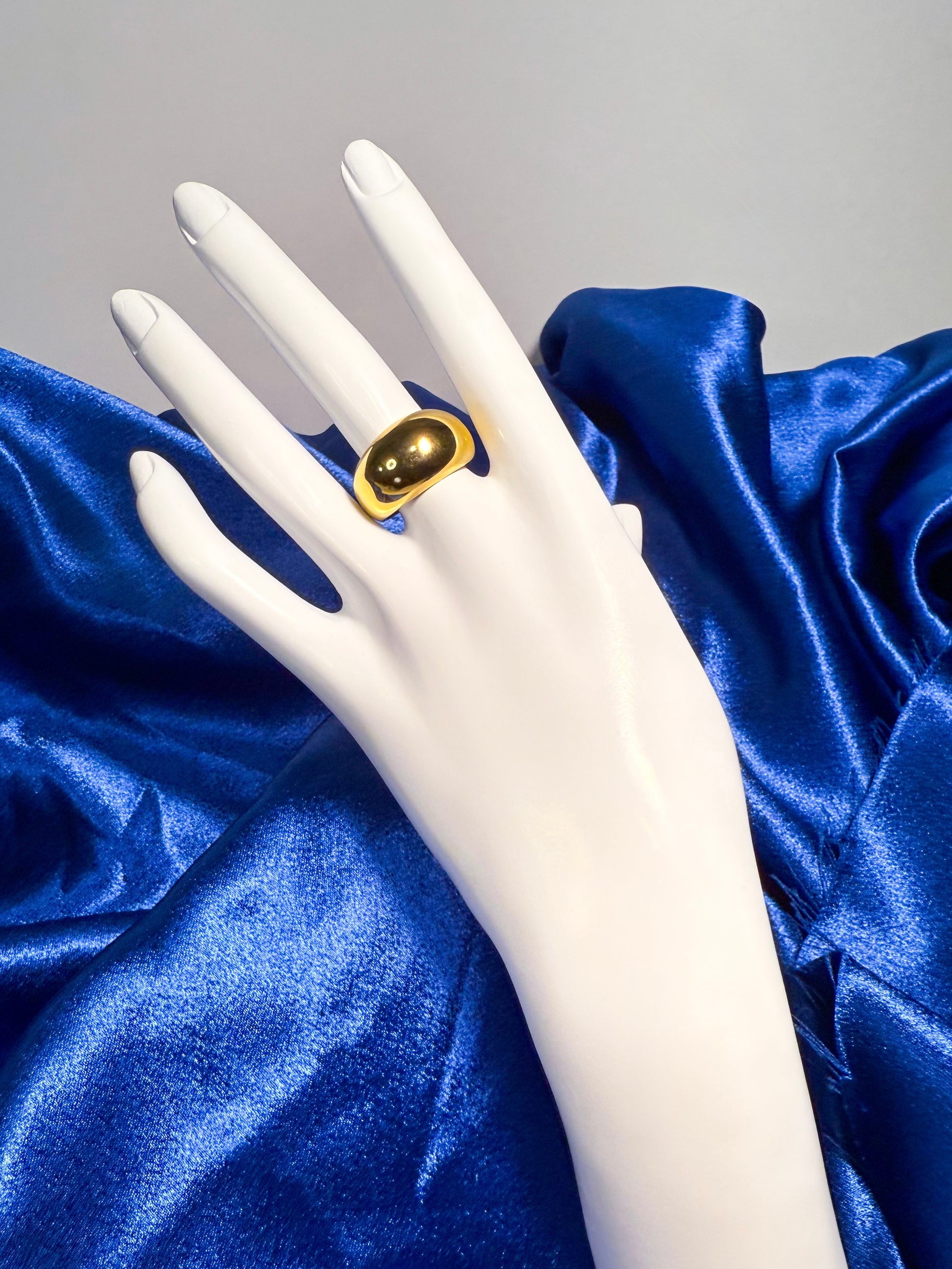 Mannequin hand wearing a gold ring on blue satin fabric
